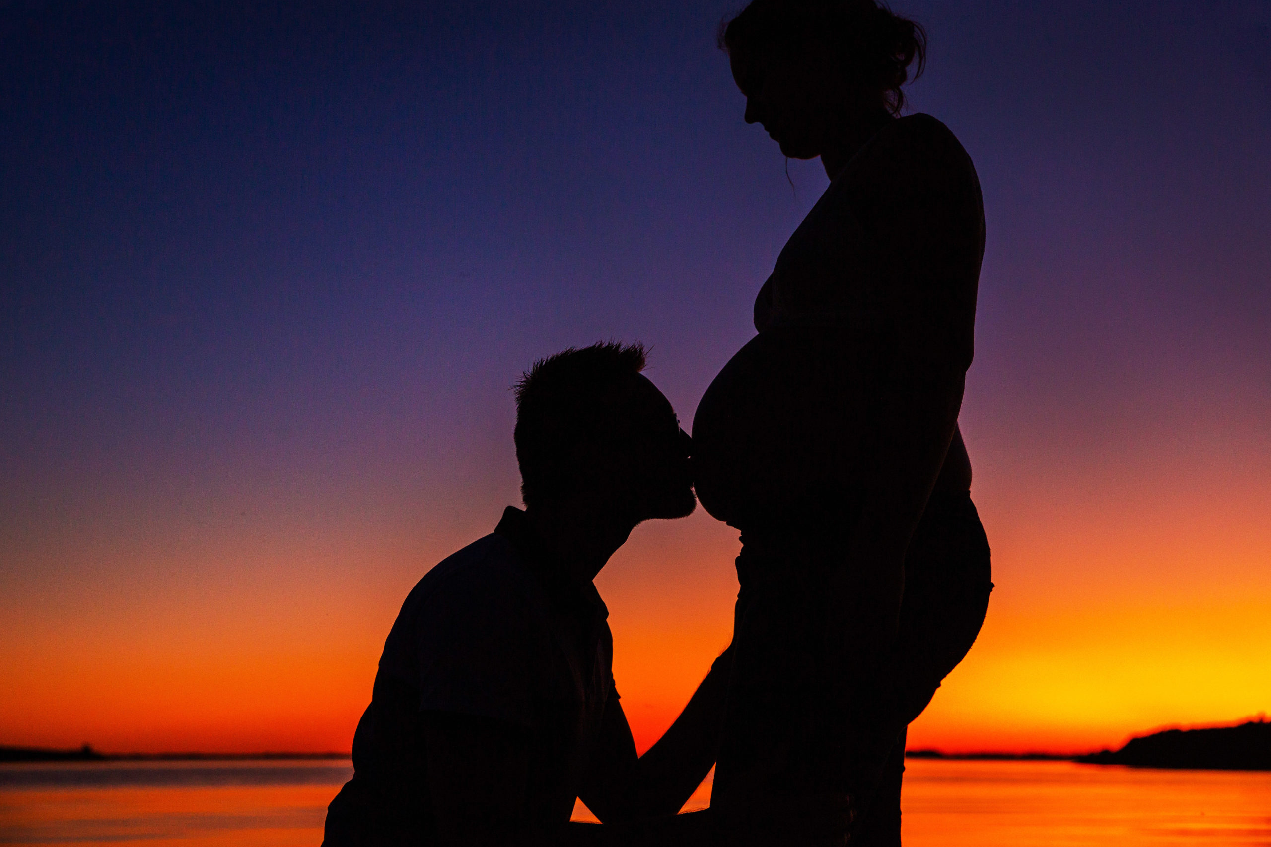 Homme faisant un bisou sur le ventre d'une femme eceinte lors d'un coucher de soleil