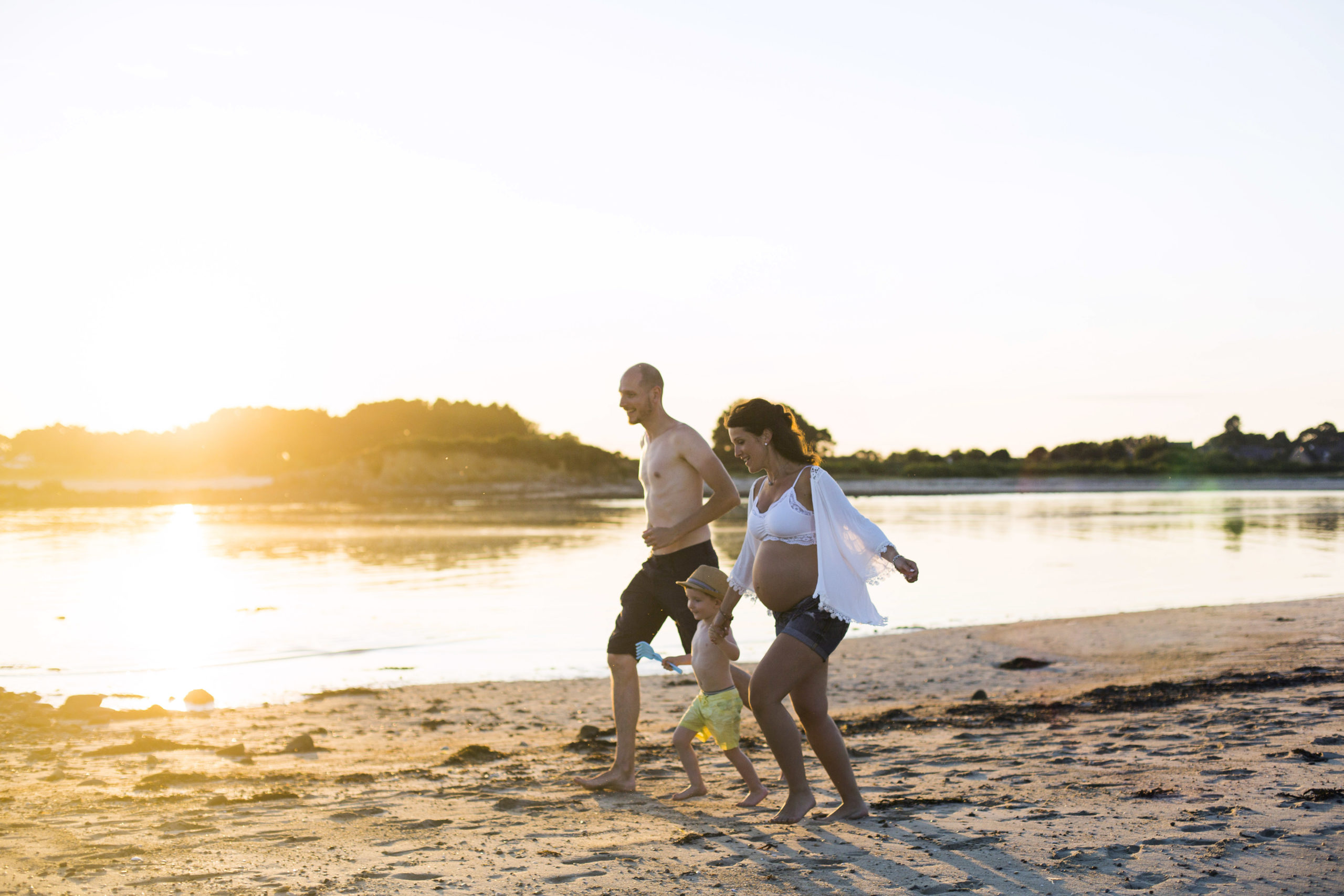 Un papa, une maman enceinte et un petit garçon courent sur la plage pendant un coucher de soleil