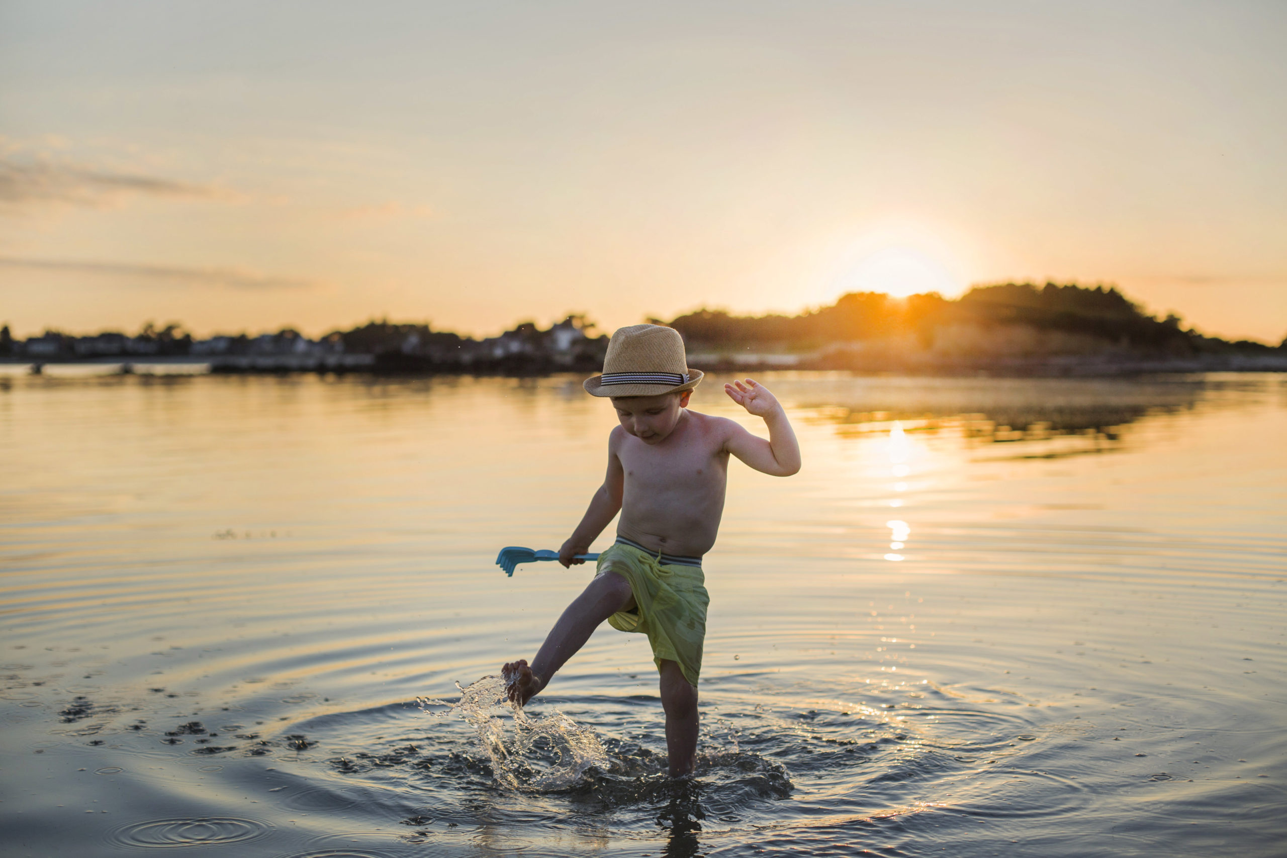 Petit garçon éclaboussant dans l'eau avec son rateau pendant un coucher de soleil